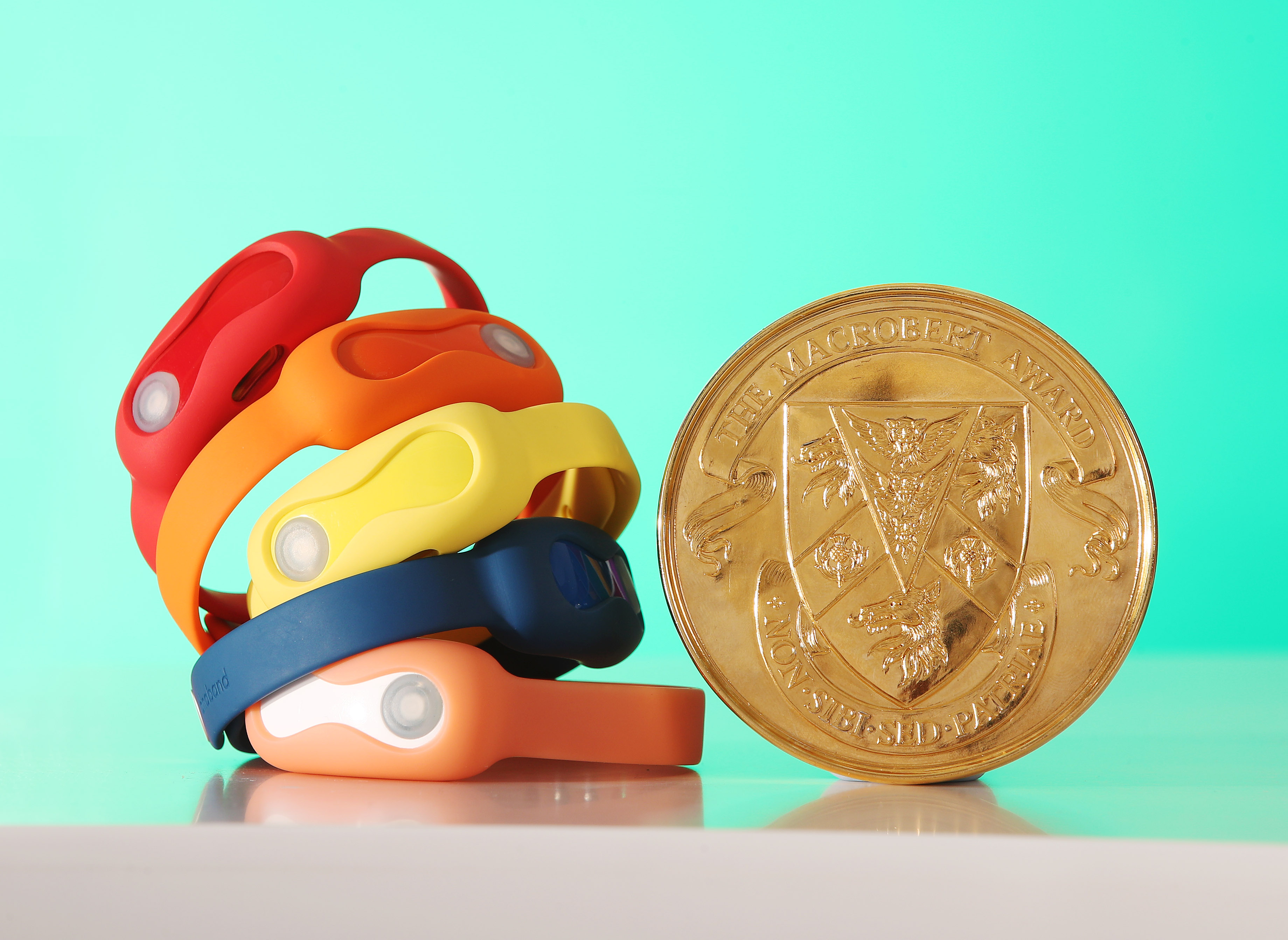 A stack of coloured DnaNudge wristbands next to a MacRobert Award medal